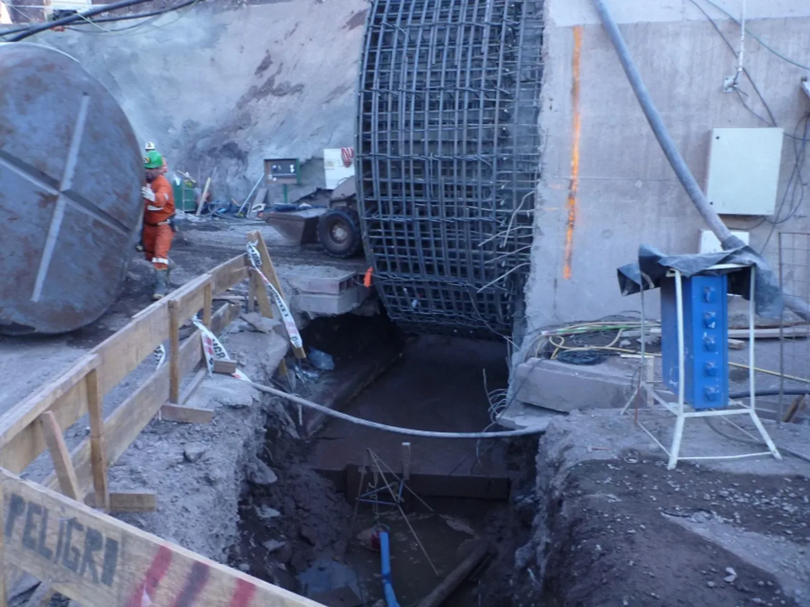 Boca del sifón con la enfierradura circular montada contra el muro de hormigón, junto a una tapa de acero apoyada en el terreno